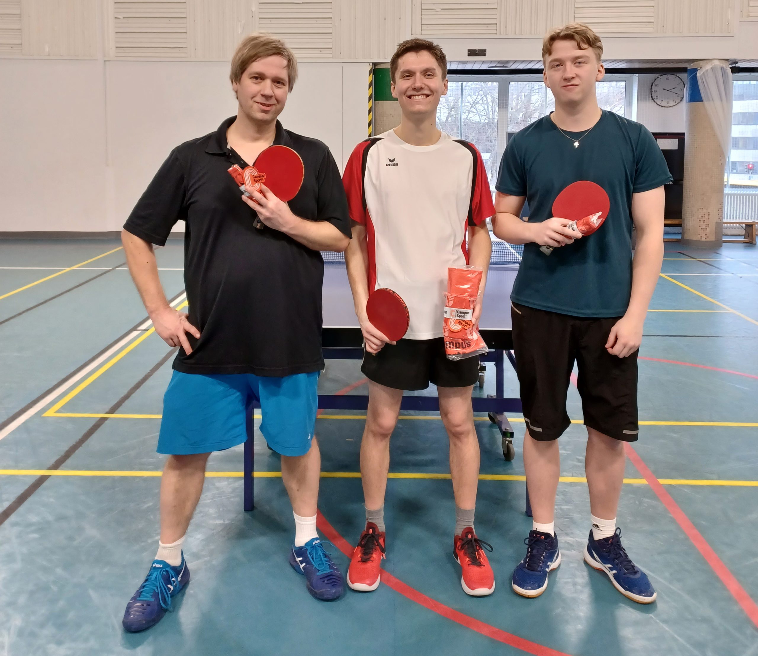The winner of men's singles series is Michael Stahl with Pasi Tolvanen who came second and Leevi Toivonen who came third. The players are in Iskeri sports hall, in front of a table tennis table, holding raquets and trophies.