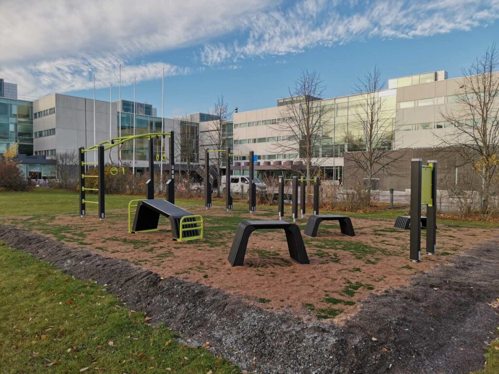 Black and green outdoor gym equipment in front of white buildings.