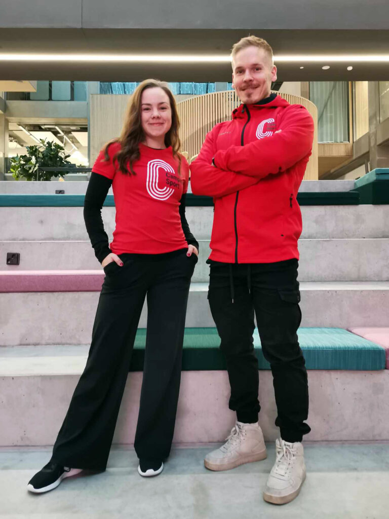 Two standing people wearing red CampusSport shirts.